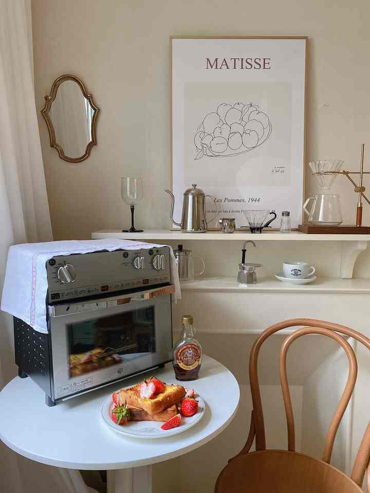Natural tones and white kitchen space featuring an air fryer oven, coffee brewing tools, and a plate of strawberry toast on a dining table in a cozy home cafe setting