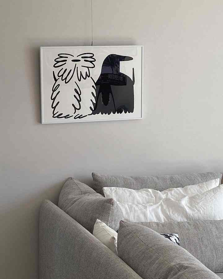 モノトーンのリビング、グレーのソファと白いクッションが配置され、壁に白黒の犬のポスターが飾られたシンプルな空間