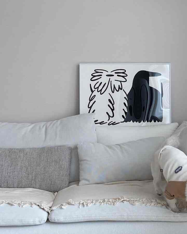 Beige and white toned living room featuring a spacious sofa with cushions, a framed poster, and a small dog