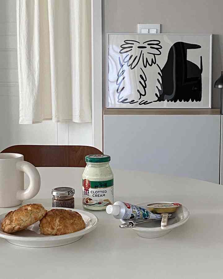 明るい白とベージュのトーンのキッチン、丸形のダイニングテーブルとポスター、カーテンが配置された落ち着いたおうちカフェの雰囲気のあるインテリア