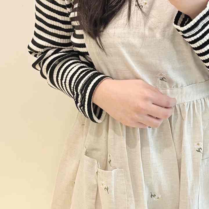 ナチュラルカラーの花柄刺繍エプロンがシンプルな背景で際立つファッションアイテム
