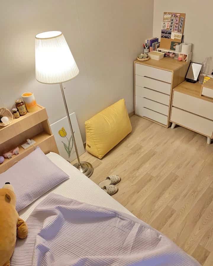 Beige and wood tone studio bedroom featuring a bed, floor lamp, and drawers with a cozy atmosphere