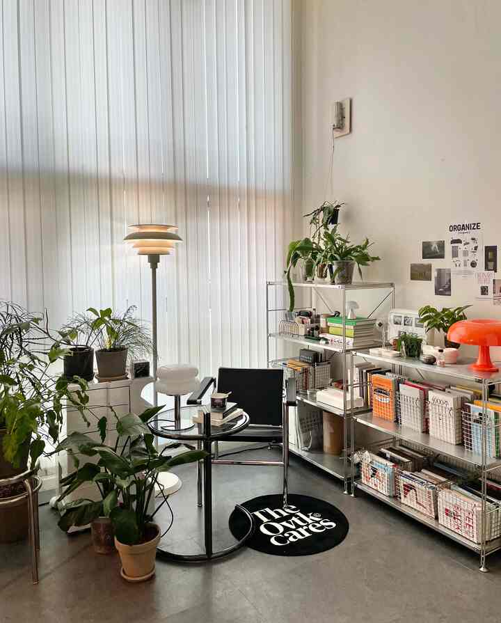 White-toned loft study space featuring stainless steel shelves and abundant plants in a modern home office interior