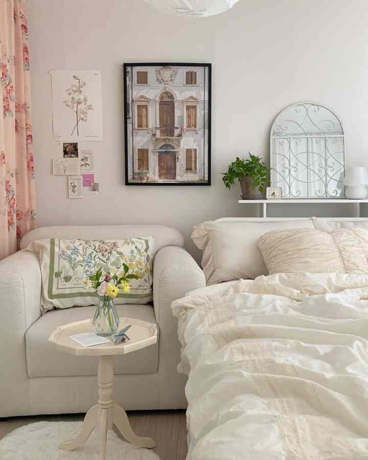Ivory and white toned bedroom featuring a bed on the right, a single armchair, floral patterned curtains, and wall-hung poster creating a cozy atmosphere