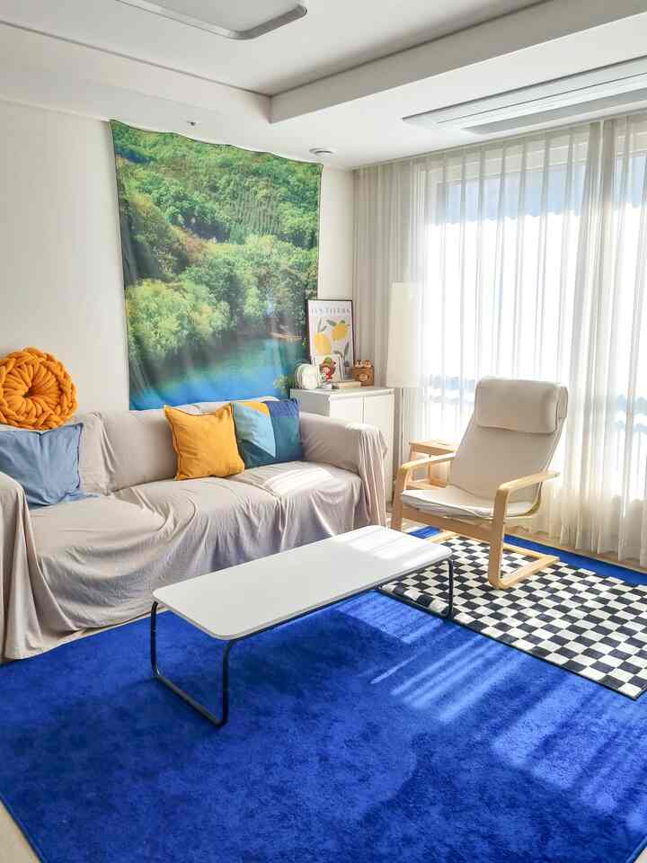 A bright living room with beige sofa and blue rug, featuring large windows letting in natural light for a cozy atmosphere