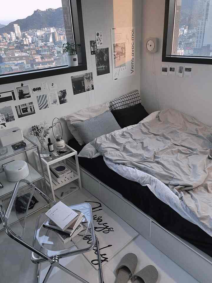 White and gray toned bedroom featuring a bed with storage, transparent chair, nightstand, and city views through large windows