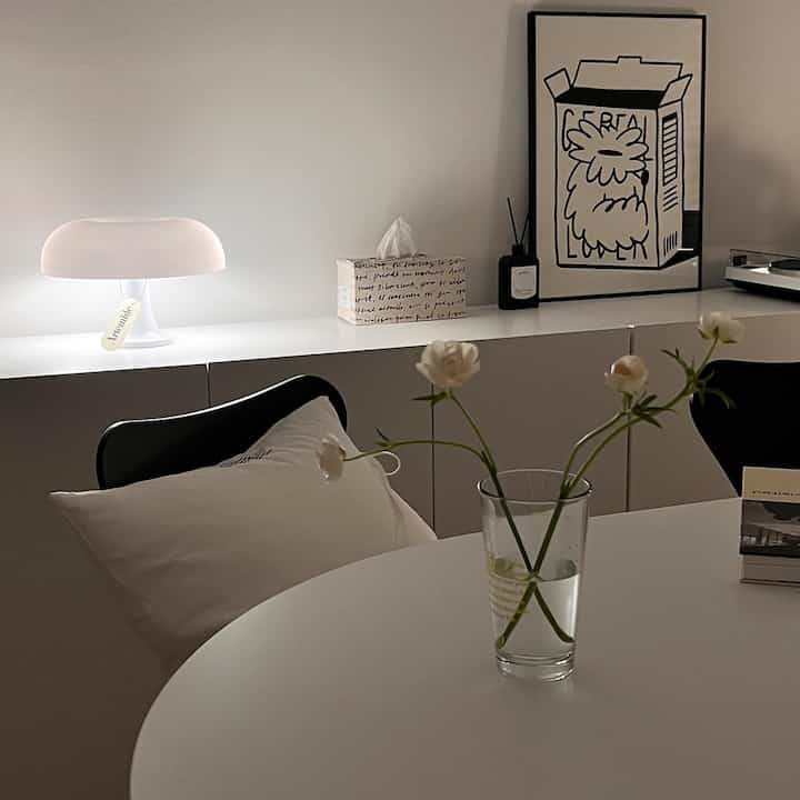 柔らかな白と黒の調和があるダイニング、中央に透明な花瓶と白いテーブルランプが配置されたモダンでミニマルなインテリア