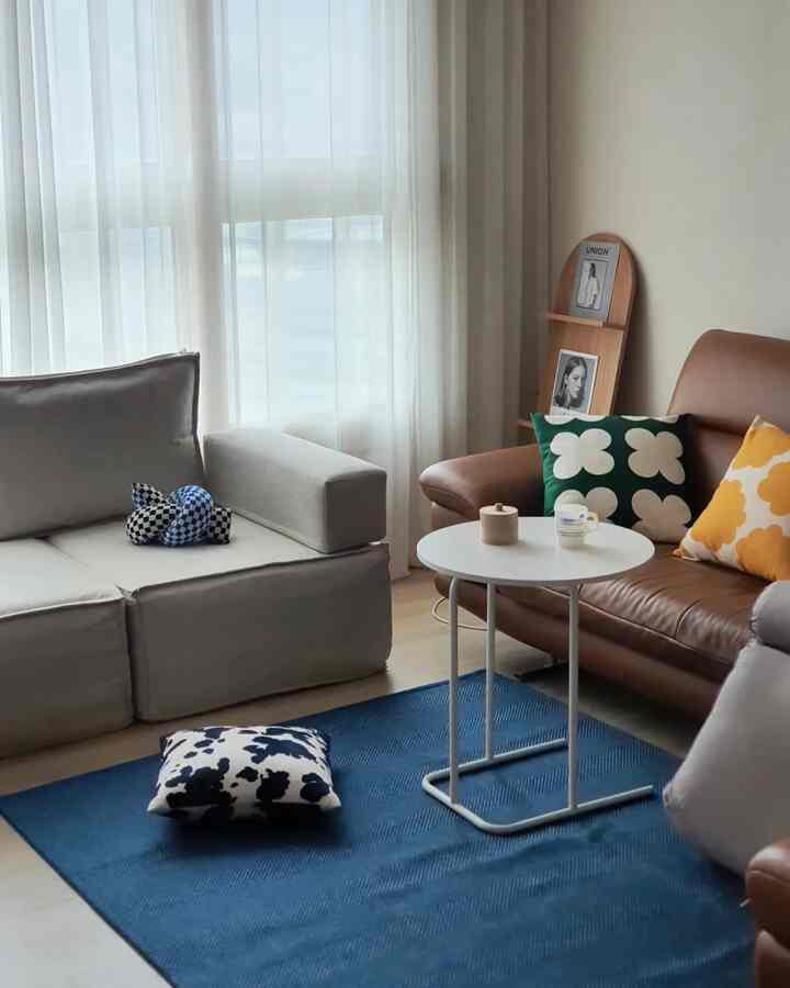 Natural-toned compact living room with white curtains and brown leather sofa featuring cushions and a blue rug