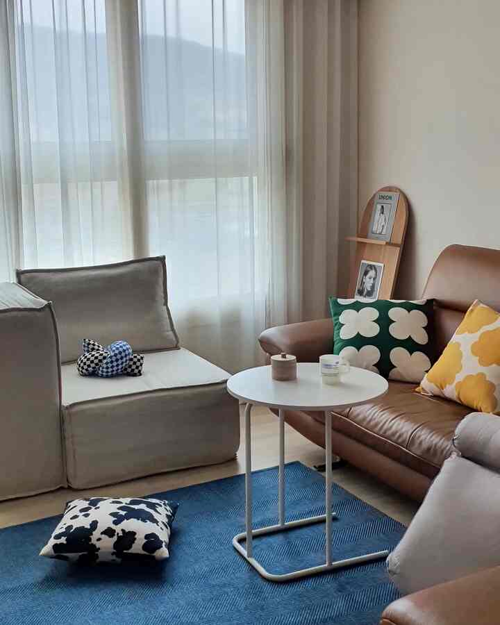 Bright living room with soft brown leather sofa, beige cushions, blue rug, and white round side table by sheer curtains