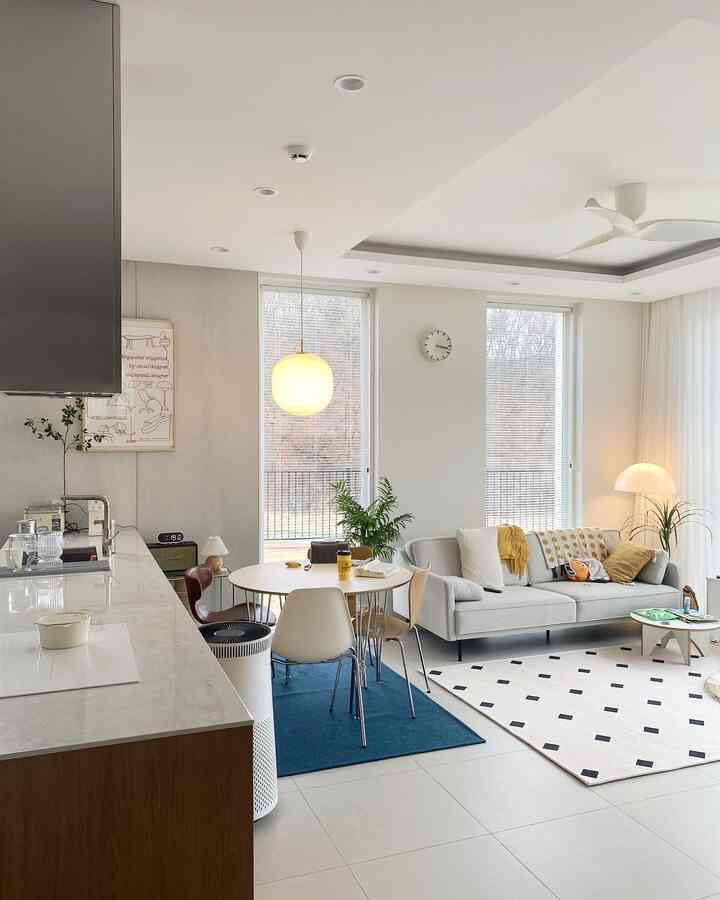 White and blue toned living room and dining area featuring a modern sofa and round dining table in a clean, bright space
