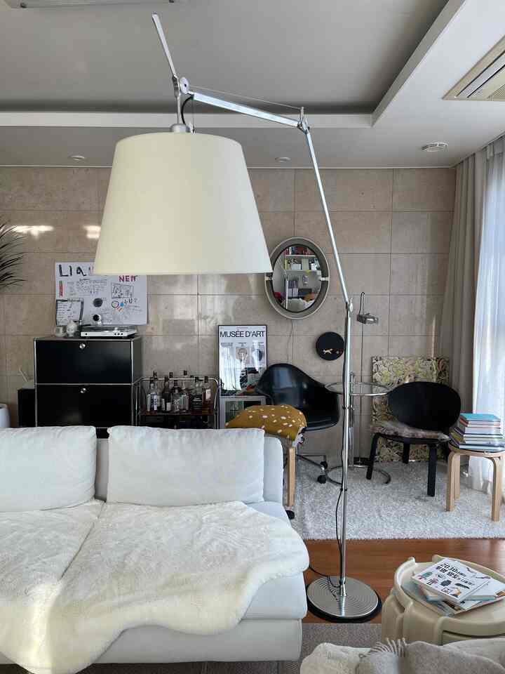White and wood-tone living room featuring mid-century modern sofa, bar cart, and floor lamp arranged in cozy setting
