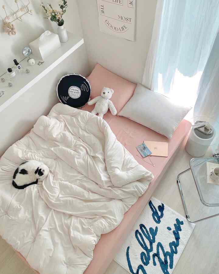 Soft white and pink toned bedroom featuring tofu-style bedding, cushions, with a cozy cat resting on the bed
