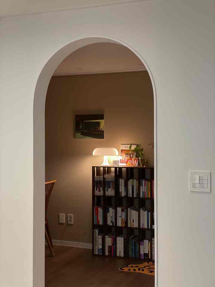 我が家の書斎であり、ダイニングルームとして使っている空間です。 
セルフインテリアを進行するとき、最も心血を傾けたプロセスは木工です。その中で一番期待していたアーチゲートを施工した空間です。 
暖かい感じだったらと思ってアーチゲートの中に見えるウォームブラウンカラーの壁紙もとても慎重に選びました。そしてアルテミデネシノとラワン本棚を置いて完成しました。この居心地の良いムードが本当に好きです。 
