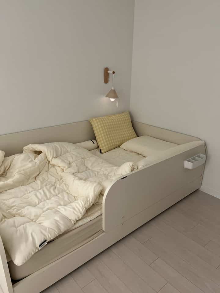 ベージュとアイボリーの色調の赤ちゃんの部屋、ゆったりとした寝具とベビーベッド、壁掛けの照明が配置された温かみのあるインテリア