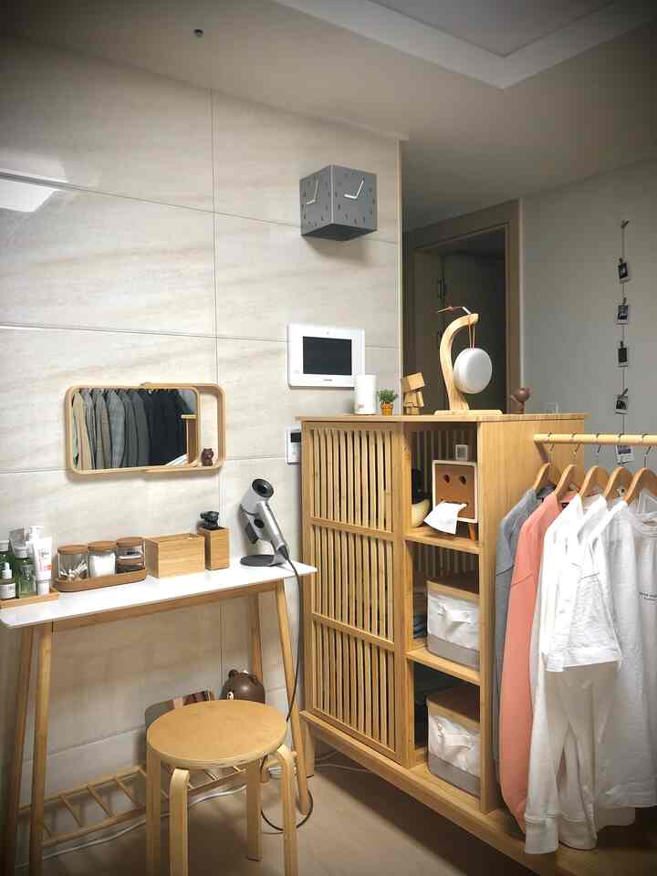 A simple vanity and wardrobe in a small space featuring beige tile walls and natural wood furniture