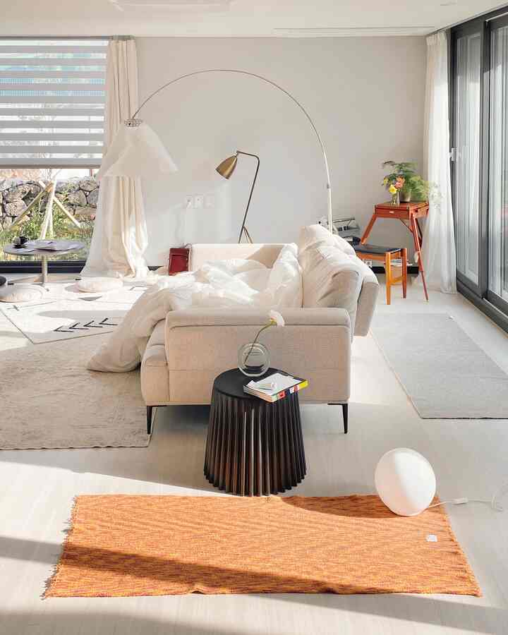 Bright white and brown toned living room featuring ivory sofa, orange rug, and floor lamp with natural, modern atmosphere