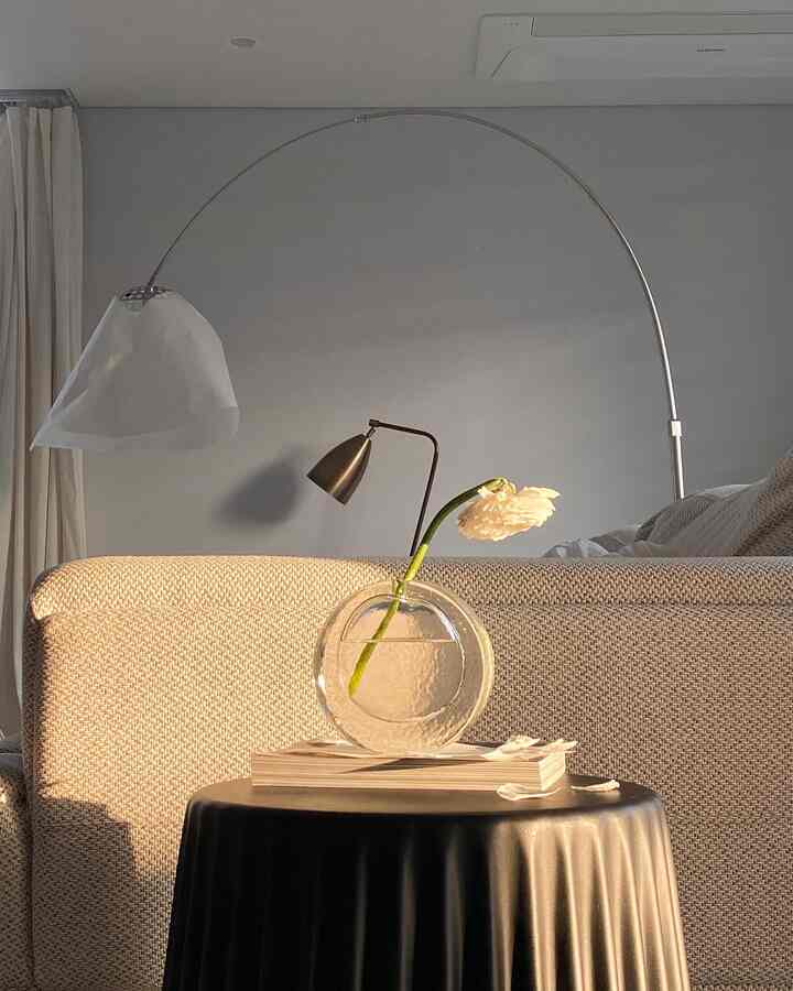 ベージュトーンのリビング、ベージュのソファ横に丸い透明な花瓶とシルバーのフロアランプが配置された暖かな雰囲気のインテリア