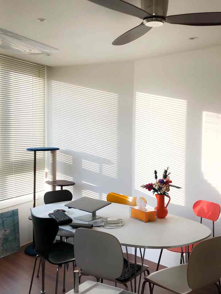 Bright white walls and brown floor create a dining space featuring colorful chairs and a cat tower, with a modern home office vibe
