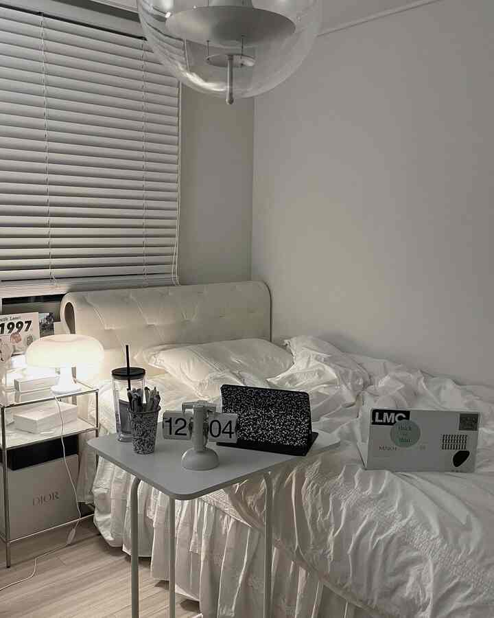 White and wood tone bedroom featuring a bed with nightstand and table lamp, presenting a cozy and practical home office atmosphere