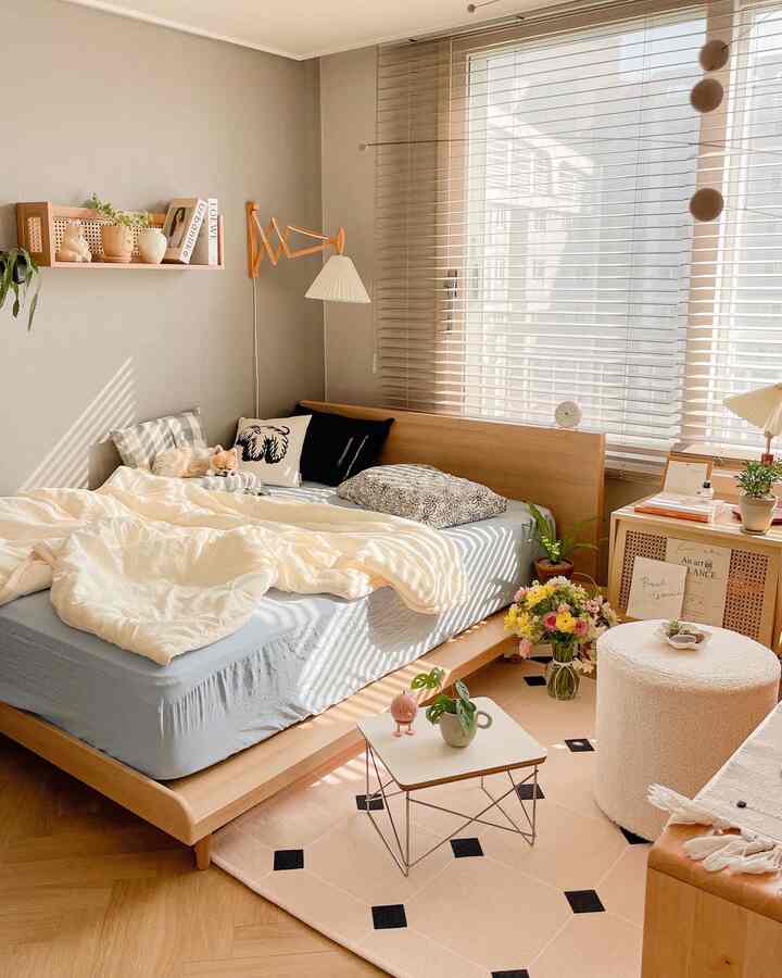 A natural-toned studio bedroom featuring a single wooden bed frame, nightstand, rug, and soft white accents with cozy atmosphere