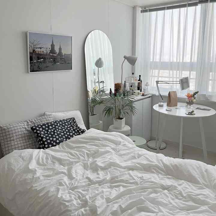 ホワイトとナチュラルカラーの寝室、ベッドとカーテン、フロアランプ、観葉植物が配置された雰囲気のあるインテリア