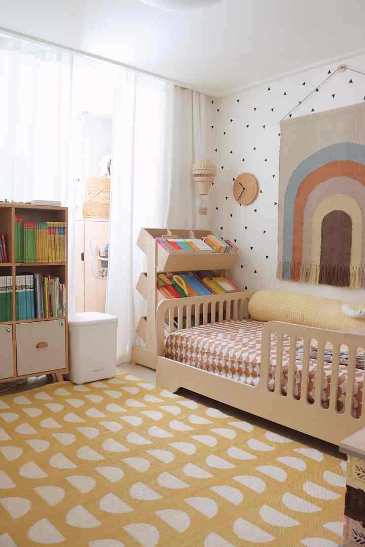 Bright natural wood-tone kids' room featuring a child's bed, toy storage, and a yellow patterned rug