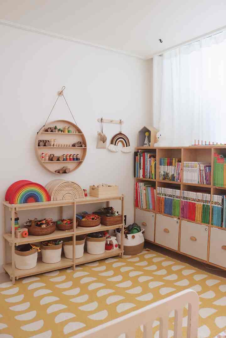 Bright kids' room with white walls and beige wooden furniture, featuring a yellow patterned rug and organized children's toys creating cozy atmosphere