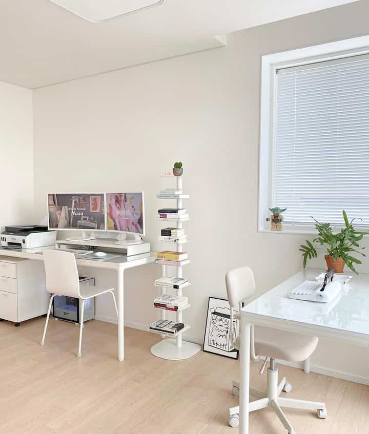 Bright white-toned study and home office space featuring dual-monitor desk, bookshelf, and wood flooring with a modern clean look