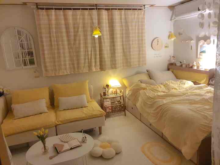 黄色とベージュのトーンでまとめられた小さなリビング兼寝室、黄色いカーテンとソファ、ベッドが印象的な雰囲気のあるインテリア