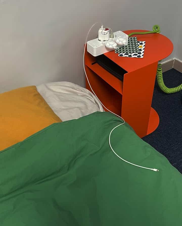 緑のベッドカバーとオレンジのナイトテーブルが配置されたミニマルな寝室