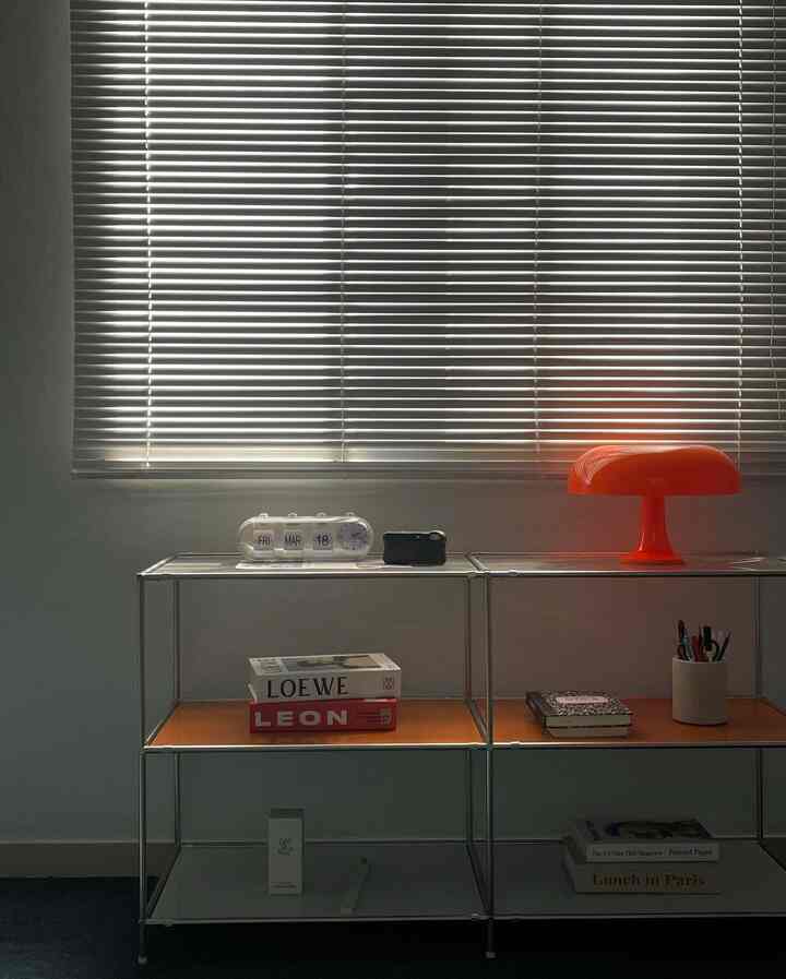 White and orange tone bedroom featuring modular shelves and a mid-century modern orange mushroom table lamp in a minimal setting