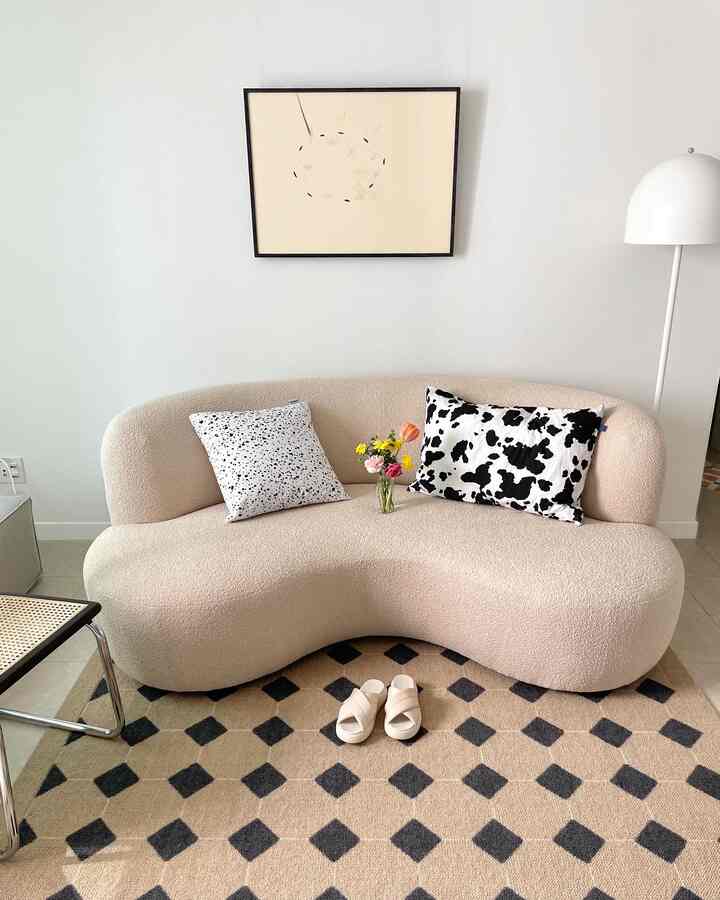 A bright beige natural living room with curved fabric sofa, black patterned cushions, harmonious rug and floor lamp arrangement