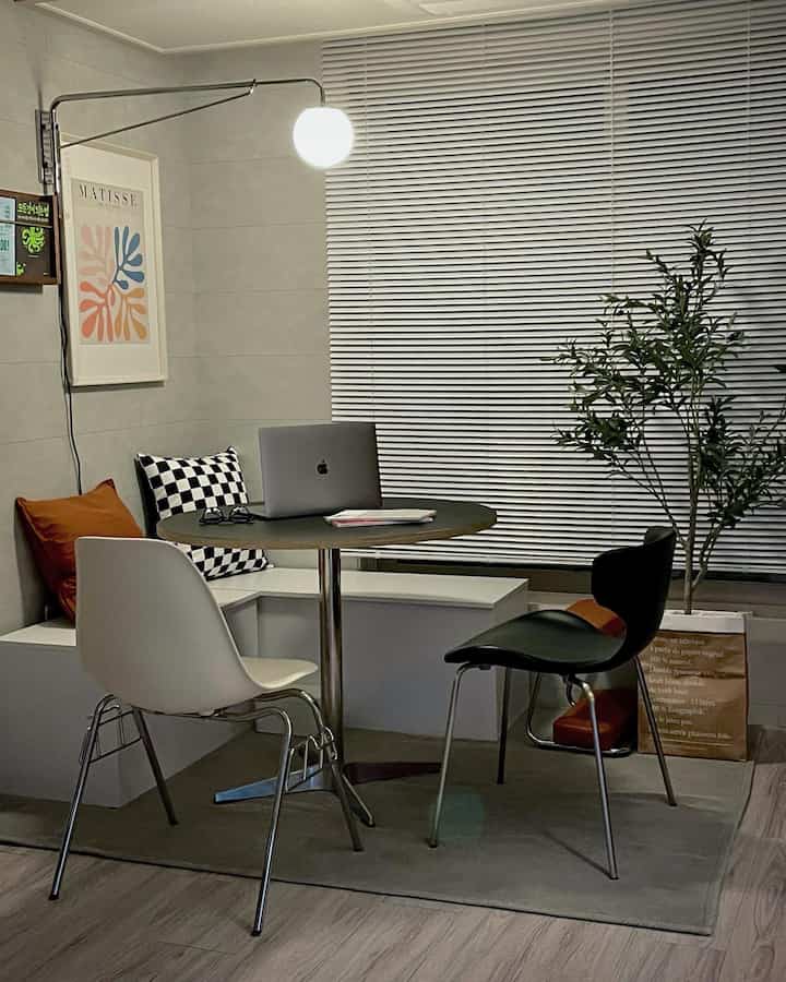 Mid-Century Modern living room with white walls and blinds, featuring a round table, bench seating, and prominent lighting creating a cozy vibe