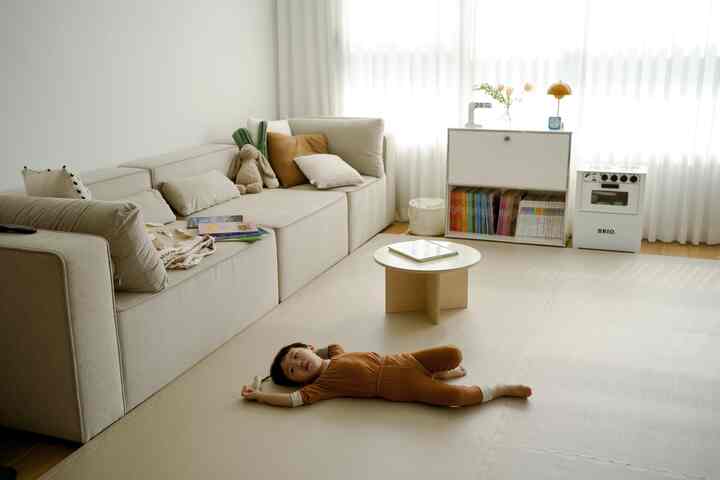 Beige-toned living room featuring a beige sofa, wooden coffee table, and a child laying on foam mat creating a cozy atmosphere