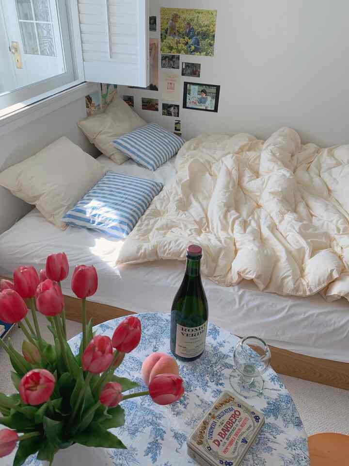 柔らかなベージュの掛け布団と白い壁が調和する寝室、赤いチューリップが飾られたテーブルが温かみのある印象的な空間を演出する