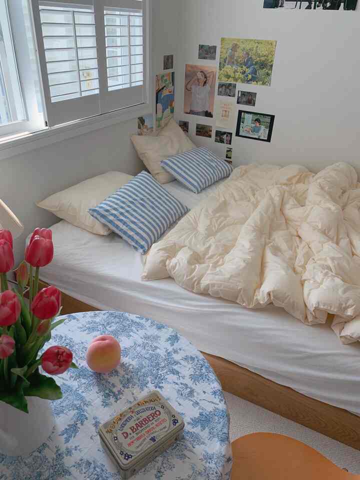 柔らかいベージュとホワイトの色調の寝室、ベージュの掛け布団とブルーストライプの枕が配された雰囲気のある空間