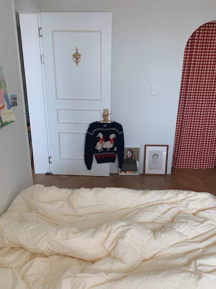 ベージュ色の掛け布団と白い壁、赤のチェック柄カーテンが配置された寝室のインテリア