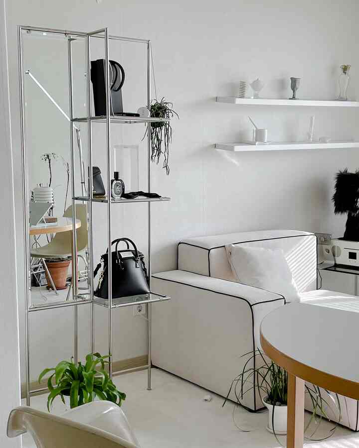 White-toned studio apartment living room featuring modern sofa and minimal shelves in a clean space
