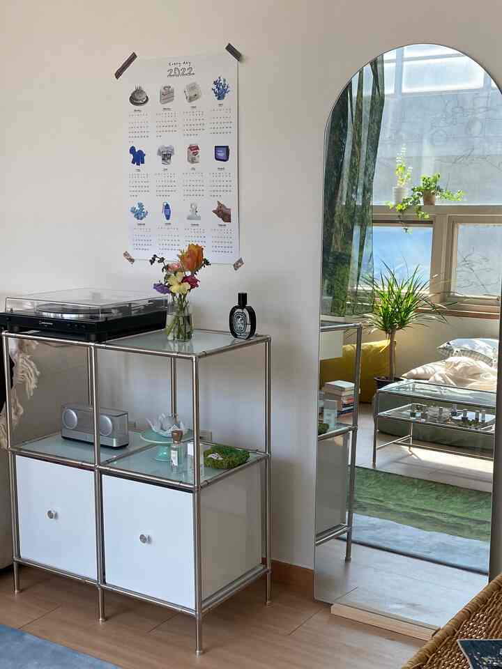 白い壁と緑のカーテンが調和するリビング、モジュール家具と全身鏡が配置されたミニマルな空間