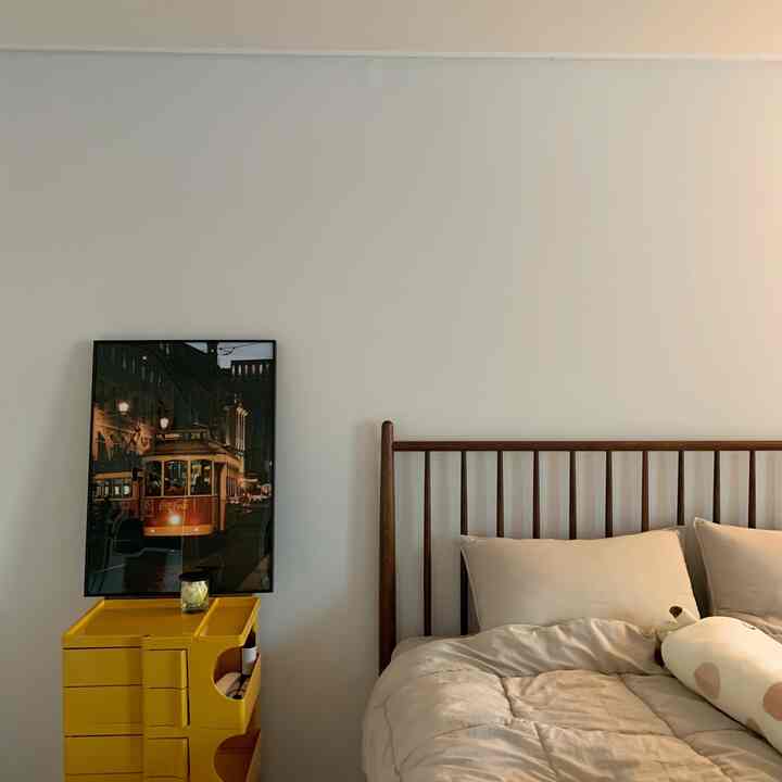 Beige-toned bedroom featuring wood-tone bed and yellow storage unit, creating a simple and cozy interior
