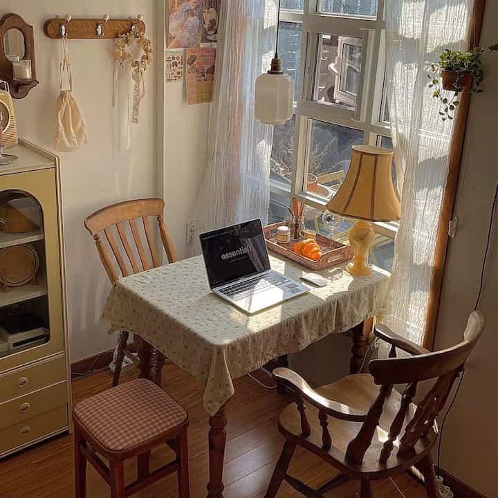 A cozy small home cafe featuring warm wood tones and natural style, with a table lamp and lace curtains creating a soft atmosphere.