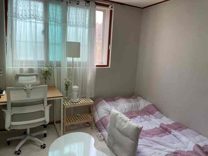 White walls and window in a small studio apartment featuring a desk and office chair, neat single household space