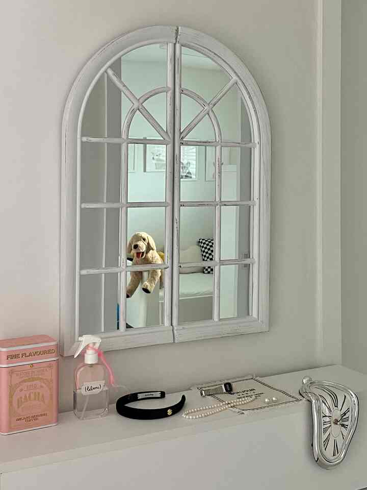 White-toned kids' room reflected in hallway mirror, featuring a stuffed dog toy and melting clock on a clean, cozy surface