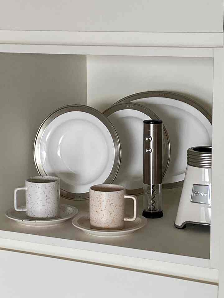 白とシルバーのトーンのキッチン棚に食器、マグカップ、ミニブレンダーが整然と配置された雰囲気のあるインテリア