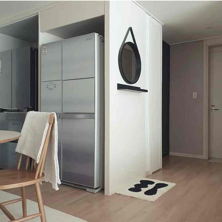 White-walled kitchen entrance featuring wood tone flooring, simple design with a refrigerator, black round mirror, and a small foot mat creating a tidy interior