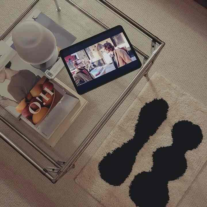 A modern, natural living room with beige and black rug flooring and a stainless steel glass table featuring an iPad on top