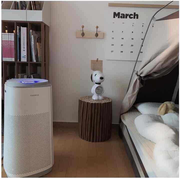 Bright white and brown toned bedroom featuring a Cuckoo air purifier and vintage bookshelf in a cozy, natural interior