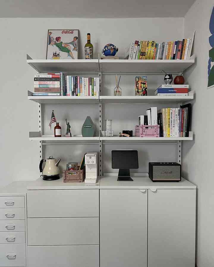 Modern white-toned home office space featuring wall-mounted shelves with organized books and decor on sleek storage cabinets
