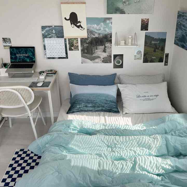 White-walled bedroom with blue and green tones, featuring a bed with pillows and a desk, creating a cozy, neat space