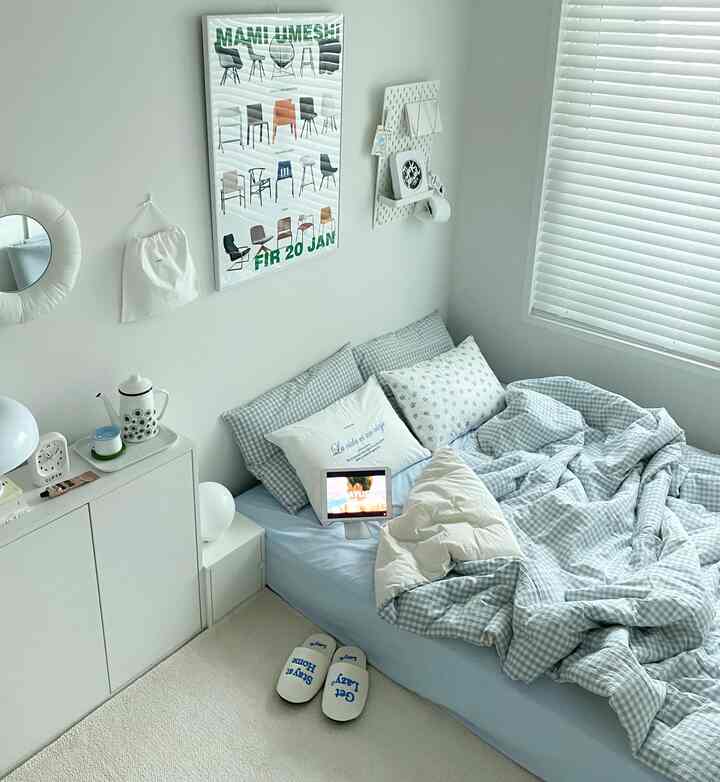 Small bedroom in white and blue tones featuring a clean bed and nightstand with a simple modern atmosphere
